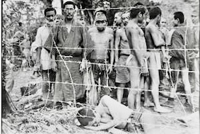 戦争捕虜のグループがフェンスの近くで立っている白黒写真