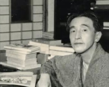 机の前に座る男性と積まれた本の画像