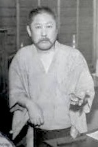男性が和服を着ている写真、手に物を持っている