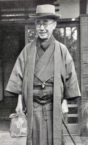 伝統的な和服を着ている男性が、帽子をかぶり、手にバッグを持っている姿