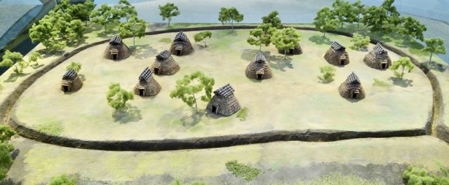 古代の集落を模したミニチュアの風景。複数の小屋があり、周囲には木々が配置されている。
