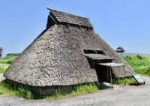 草葺き屋根の伝統的な日本の住居、青空と緑の草地に囲まれている